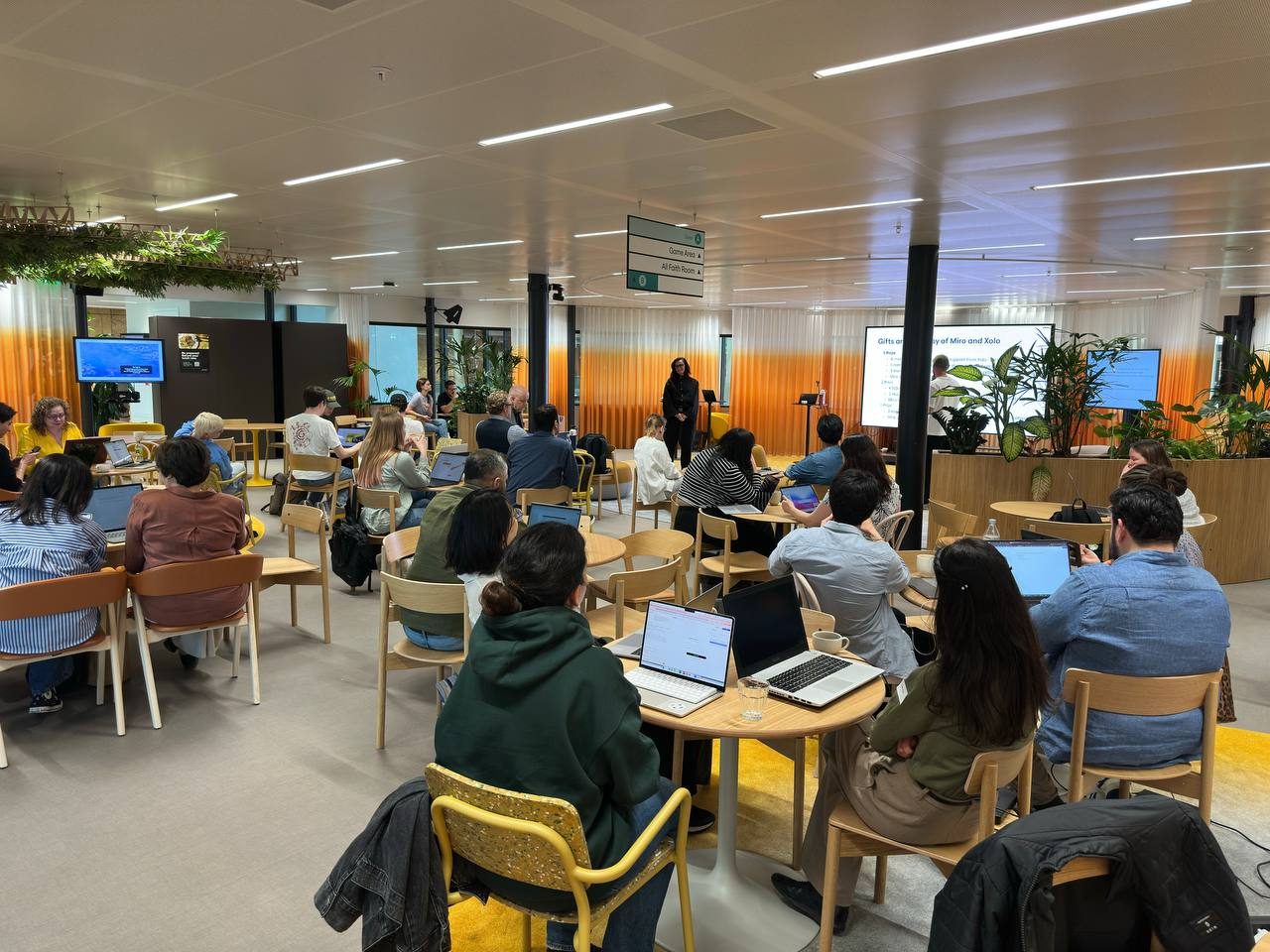Builders working at tables during the Miro × Lovable Buildathon in Amsterdam, with a presentation at the front of the room.